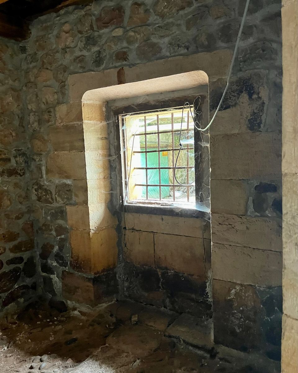 Dentro del cuarto: muros de piedra y una ventana pequeña con reja